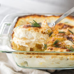 A scoop of Au Gratin potatoes being taken out of a baking dish with a large metal serving spoon
