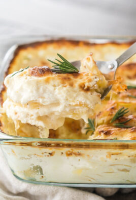 A scoop of Au Gratin potatoes being taken out of a baking dish with a large metal serving spoon