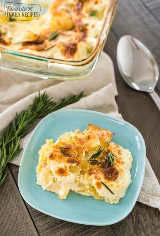 A plate of au gratin potatoes next to a baking dish of au gratin potatoes