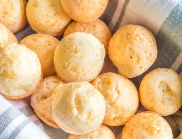 Brazilian cheese bread rolls in a basket, about a dozen small rolls.