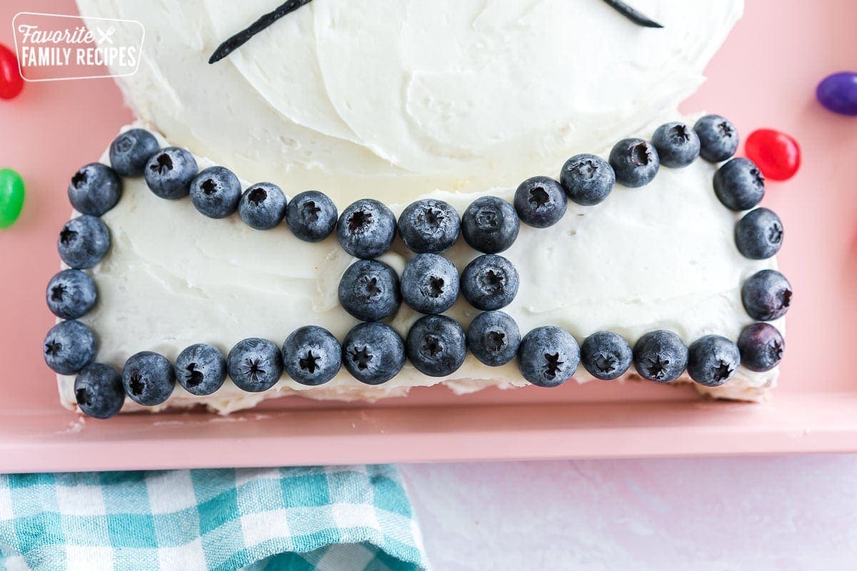 A bowtie made out of cake with white frosting and decorated with blueberries