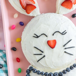 A bunny cake on pink baking sheet surrounded by jelly beans