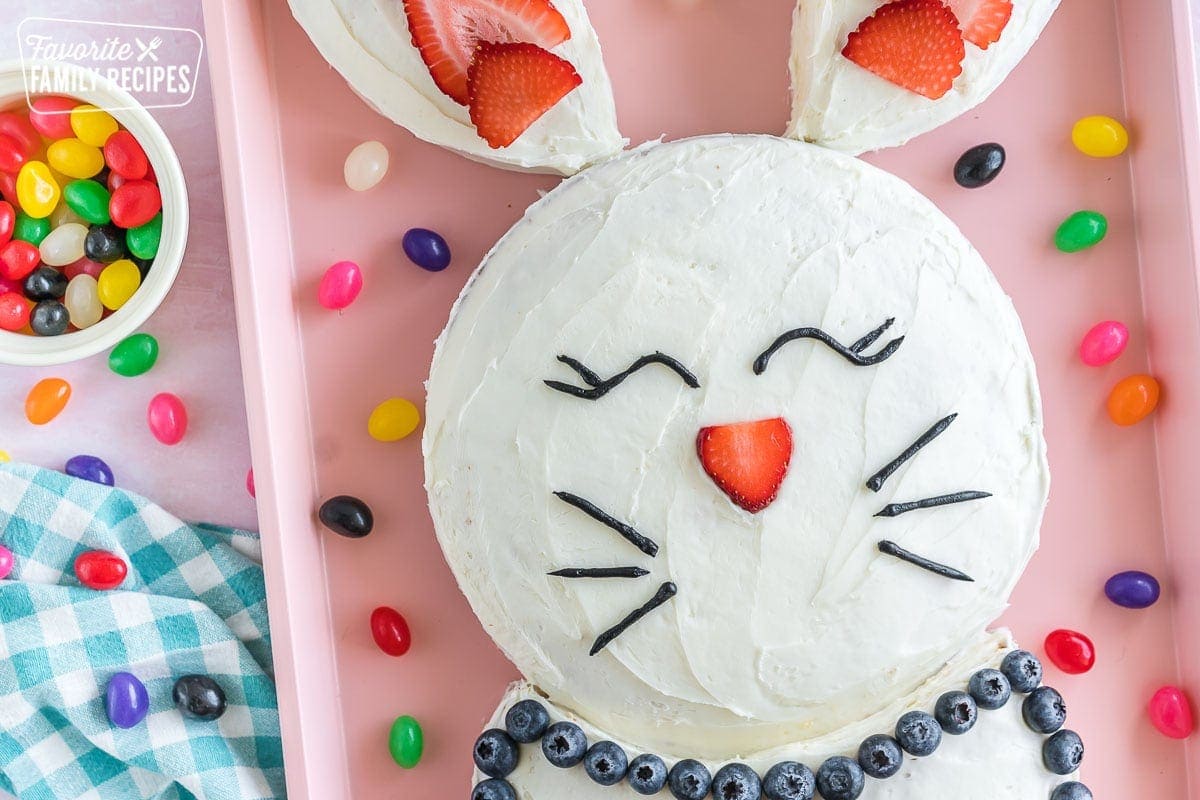 A bunny cake on pink baking sheet surrounded by jelly beans.