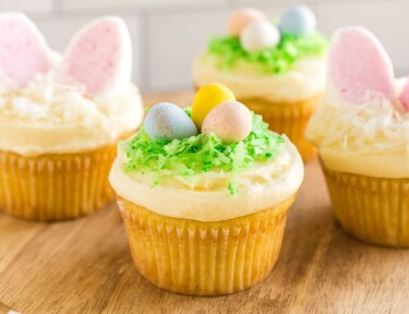 Easter cupcakes on a wooden cupcake stands. Some of the cupcakes have birds nests made out of candy and the others have bunny ears made out of marshmallows