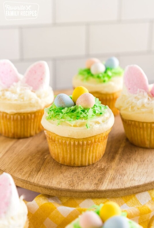 Easter cupcakes on a wooden cupcake stands. Some of the cupcakes have birds nests made out of candy and the others have bunny ears made out of marshmallows