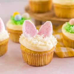 An Easter Cupcake sprinkled with coconut and topped with two bunny ears made out of marshmallows and pink sprinkles