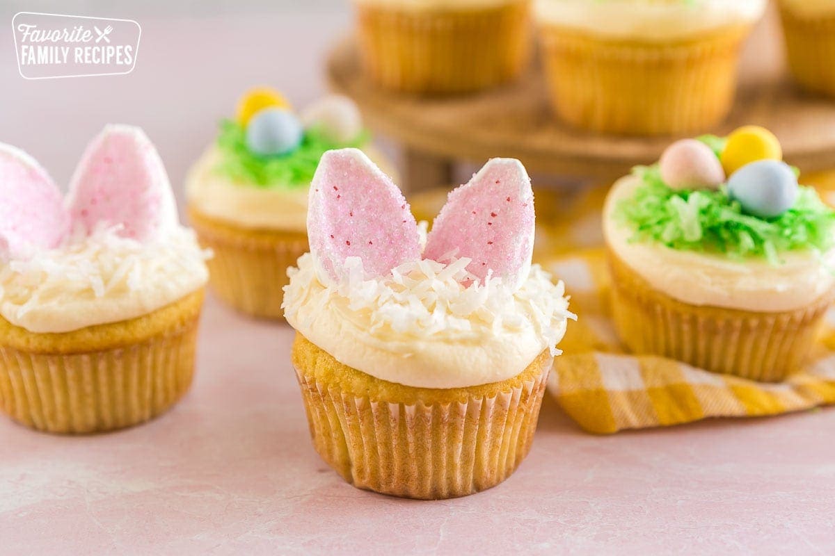 An Easter Cupcake sprinkled with coconut and topped with two bunny ears made out of marshmallows and pink sprinkles