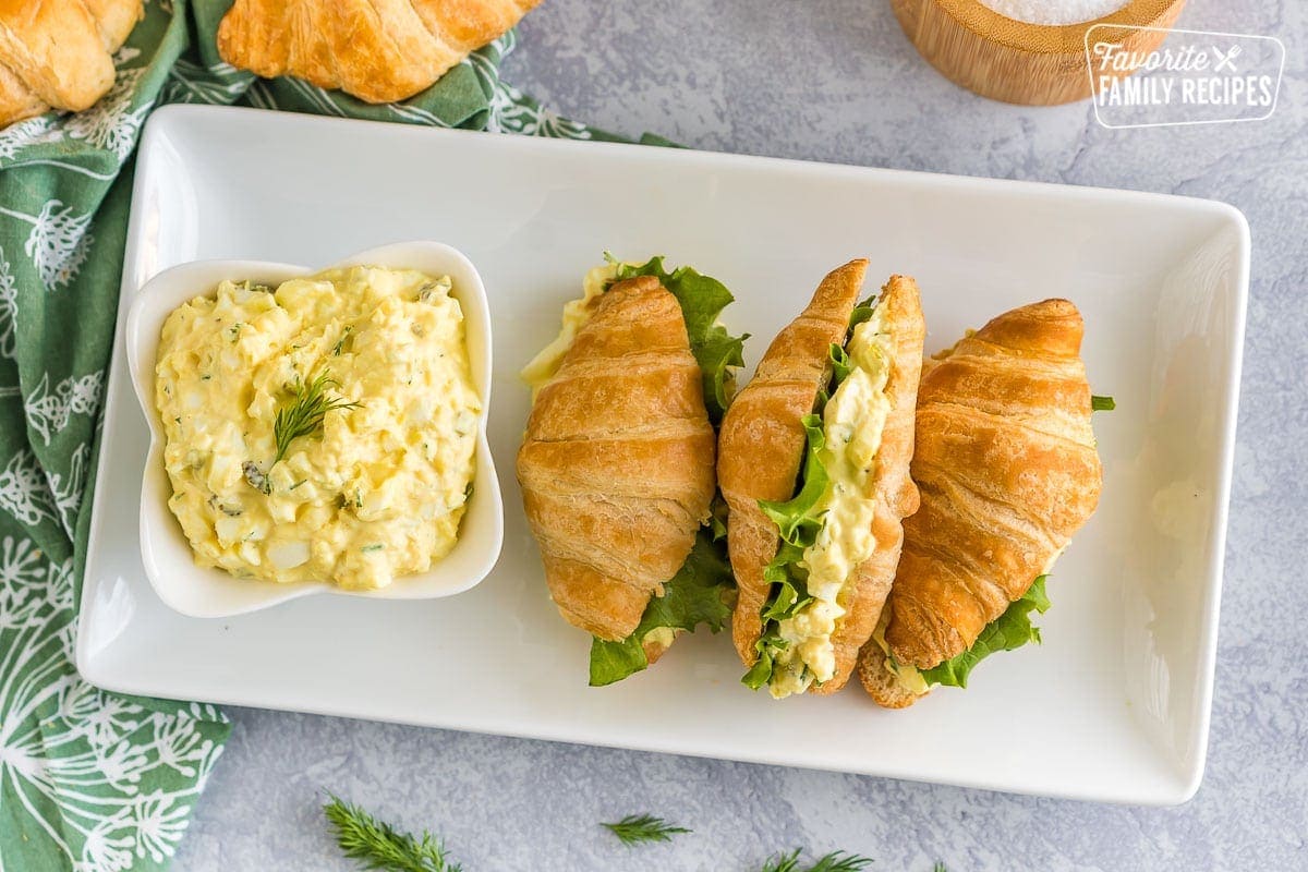 A platter of egg salad sandwiches and each egg salad sandwich is made on a croissant with a slice of lettuce