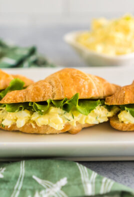 Three Egg Salad Sandwiches on a white platter. Each egg salad sandwich is made on a croissant with a slice of lettuce on top