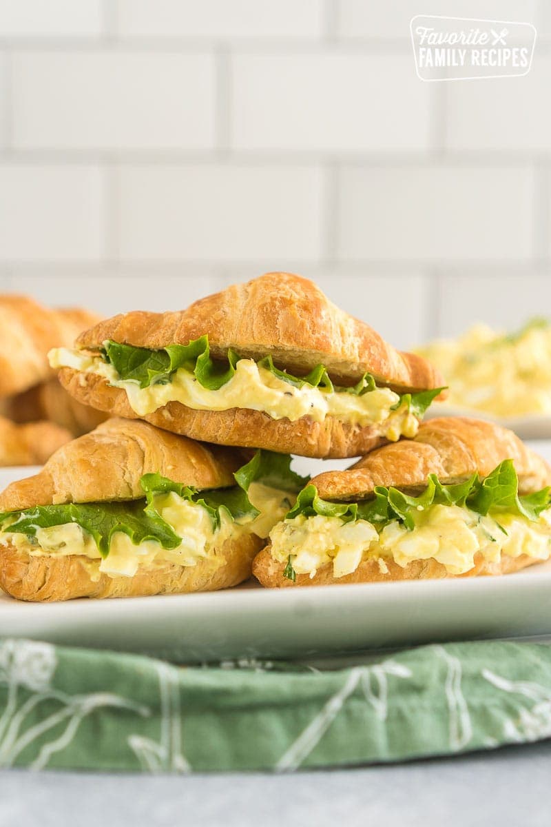 Three Egg Salad Sandwiches stacked on a white platter.