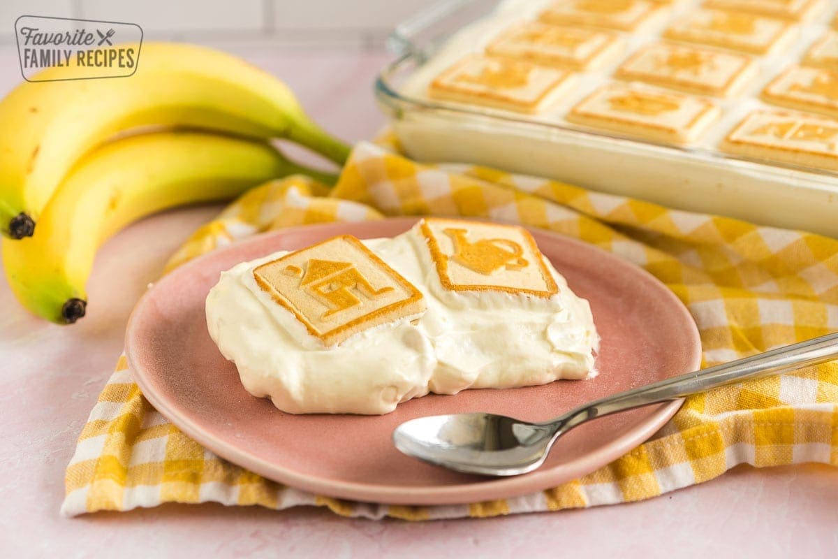 A scoop of banana pudding on a pink plate with two bananas in the background.