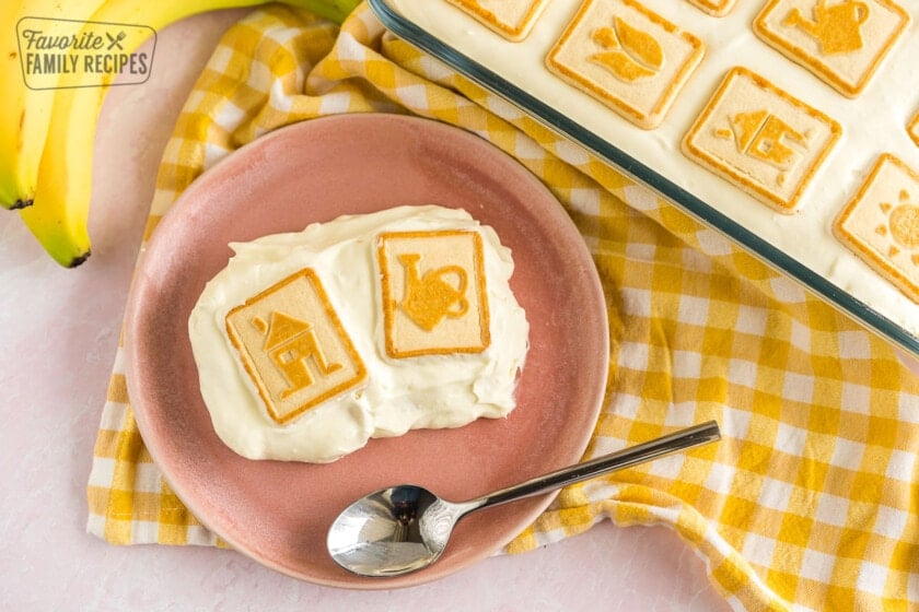 A scoop of banana pudding on a pink plate with two bananas in the background