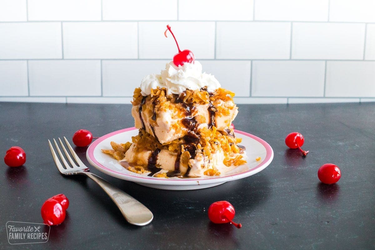 A plate of fried ice cream cake with a corn flake topping, ice cream toppings, and cherries