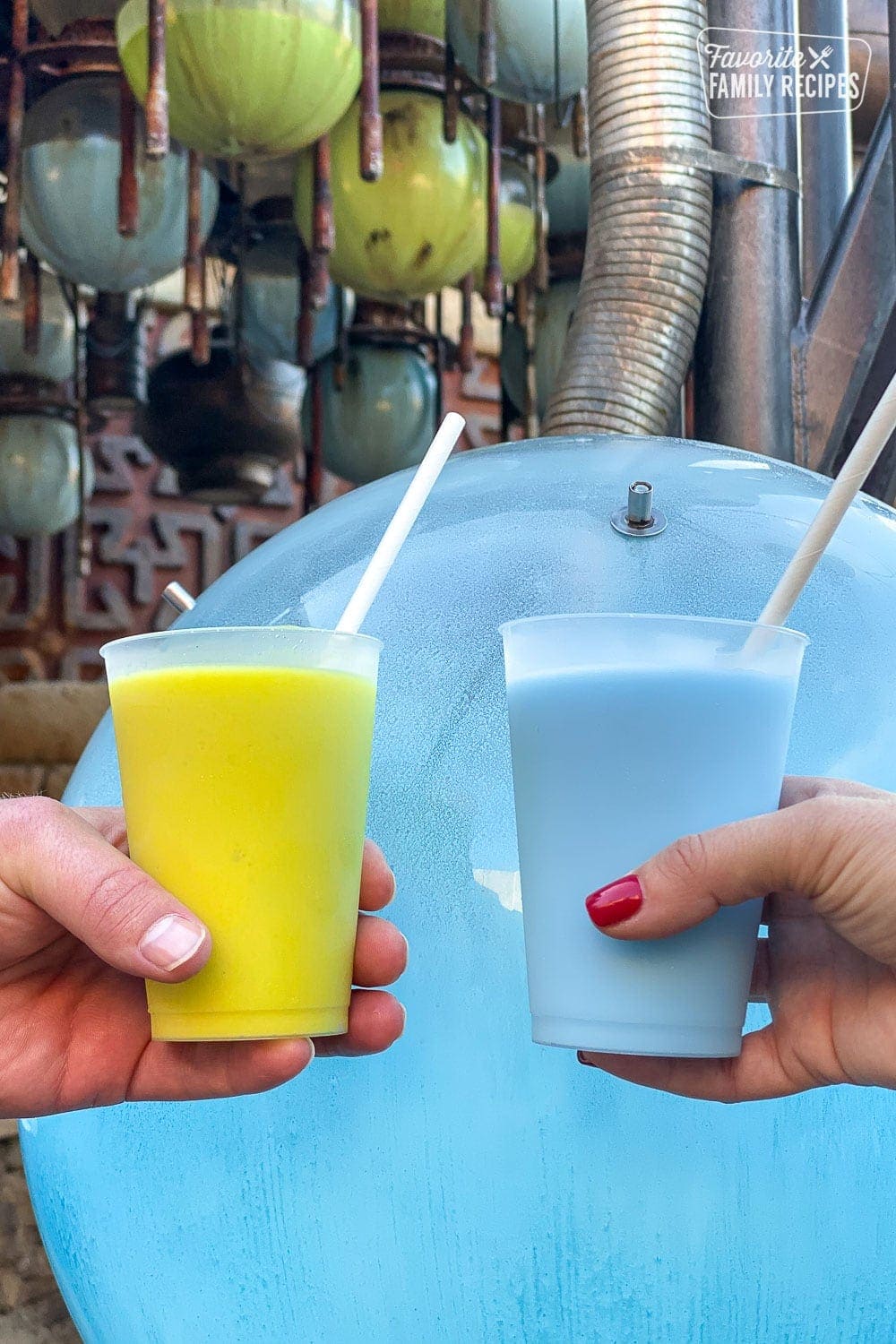 A cup of green milk and blue milk being held next to each other. 