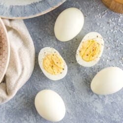 Peeled Hard Boiled Eggs on a plate with one egg cut in half and sprinkled with salt and pepper