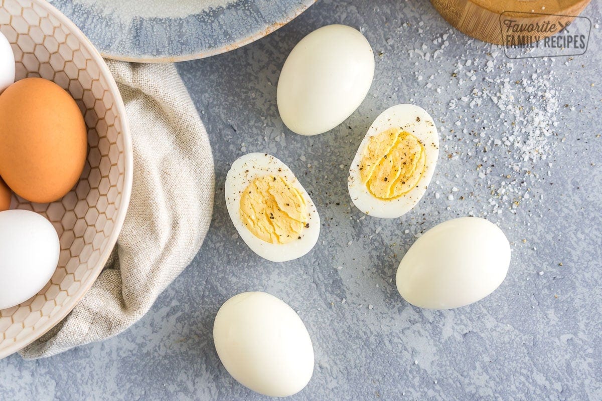 Peeled Hard Boiled Eggs on a plate with one egg cut in half and sprinkled with salt and pepper