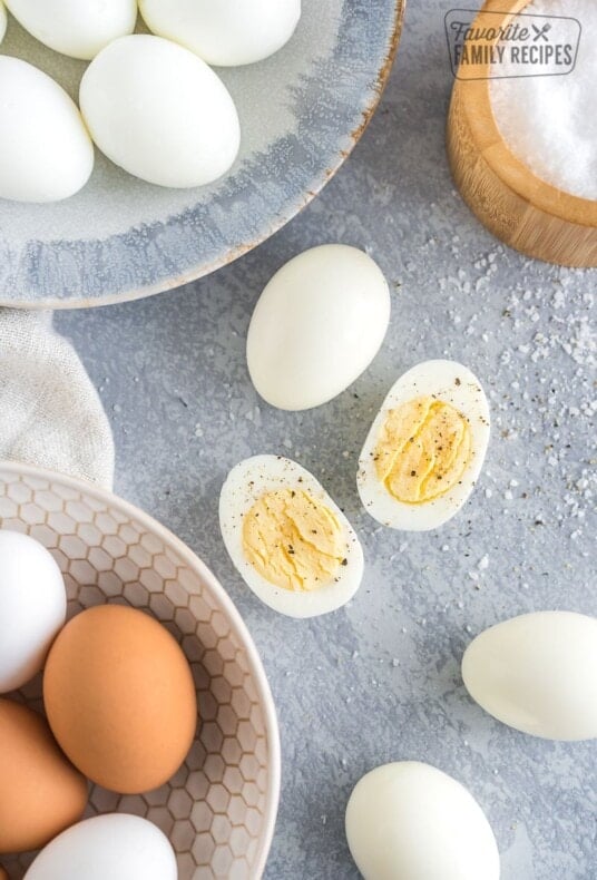 Peeled Hard Boiled Eggs on a plate with one egg cut in half and sprinkled with salt and pepper