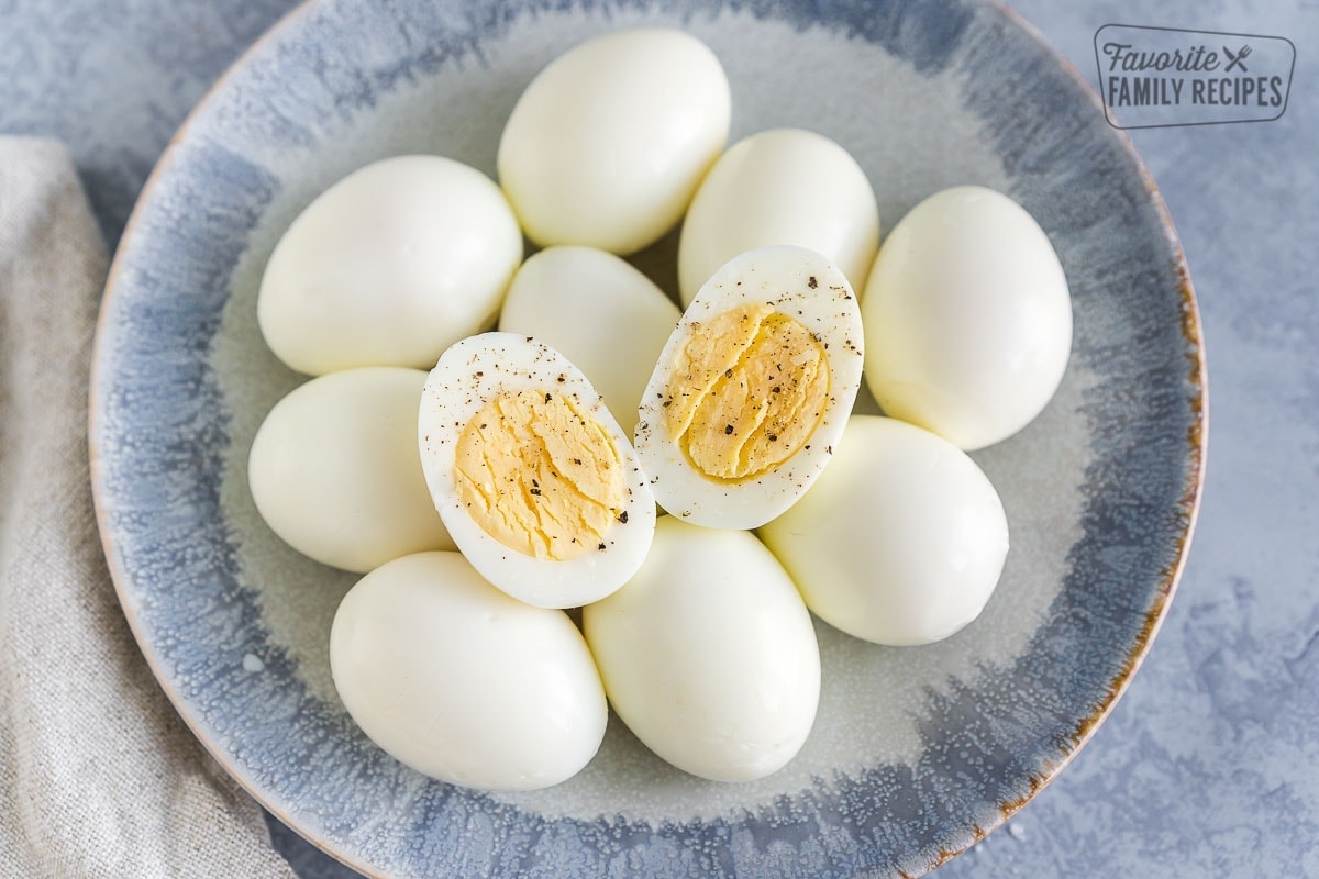 Peeled Hard Boiled Eggs on a plate with one egg cut in half and sprinkled with salt and pepper