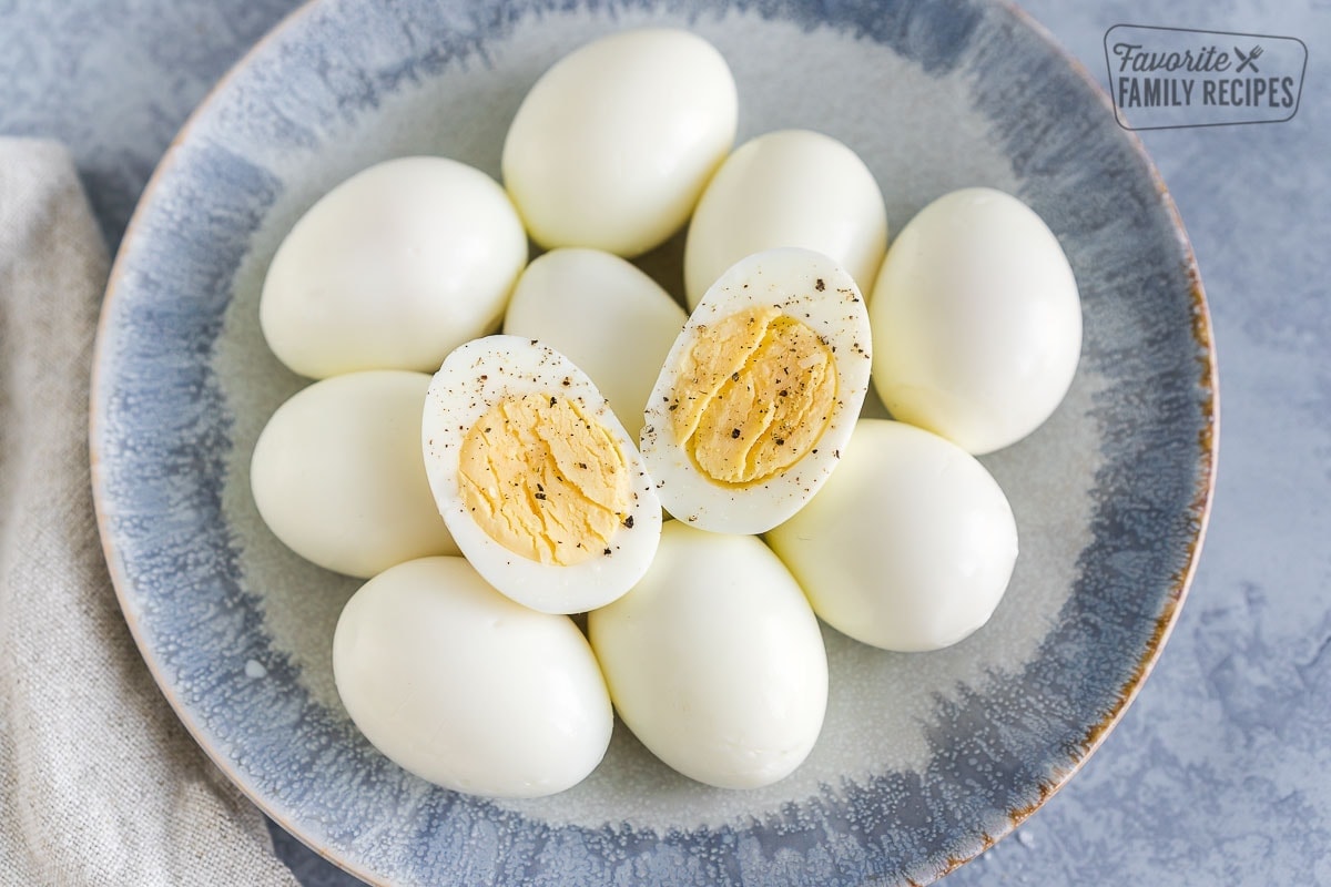 Peeled Hard Boiled Eggs on a plate with one egg cut in half and sprinkled with salt and pepper.