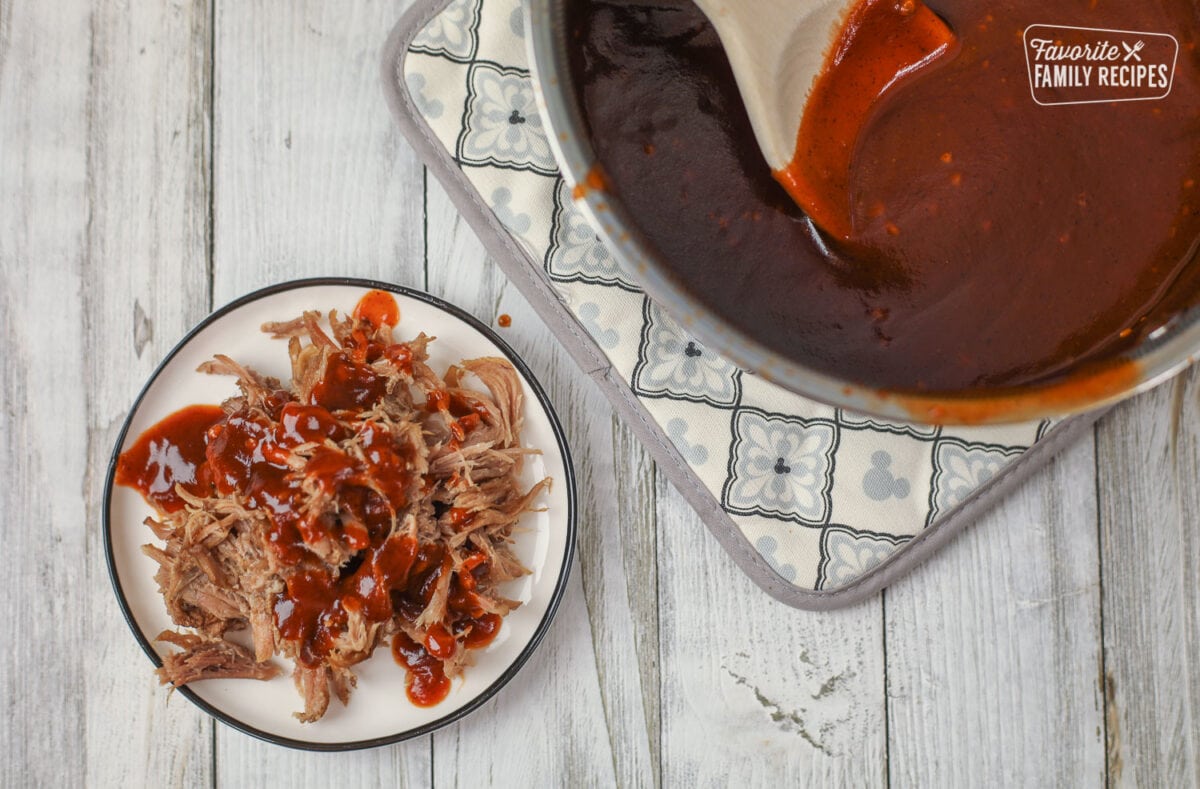 Plate of pulled pork with BBQ Sauce next to a sauce pan of BBQ Sauce.