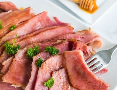 Sliced honey baked ham on a platter next to a bowl of honey