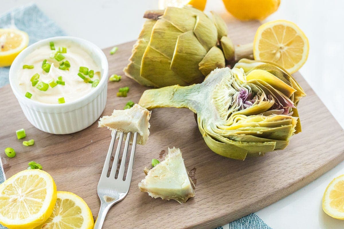 An artichoke heart on a fork that is sitting on a cutting board with cooked artichokes