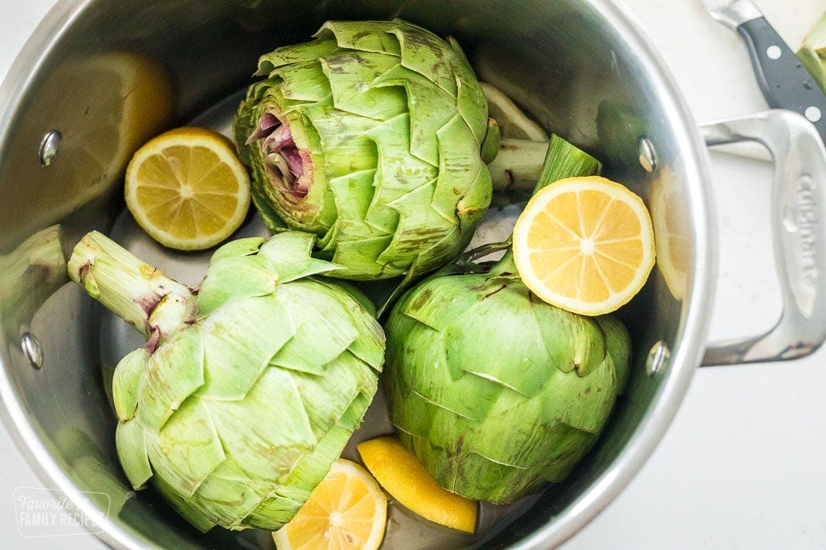 Three uncooked artichokes in a pot with lemons