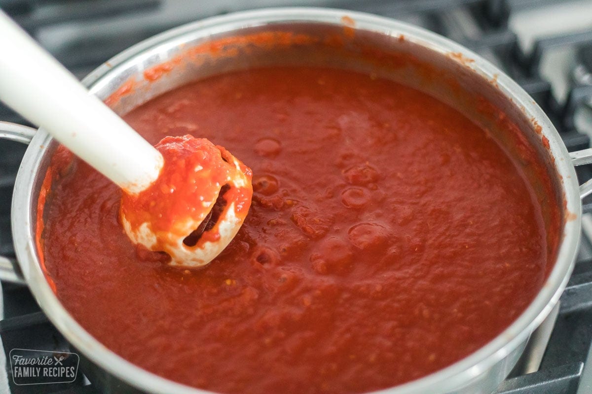 An immersion blender blending tomatoes in a pan