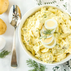 Potato salad in a large bowl next to potatoes and a hard boiled egg