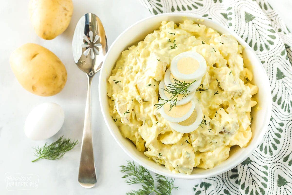 Potato salad in a large bowl next to potatoes and a hard boiled egg
