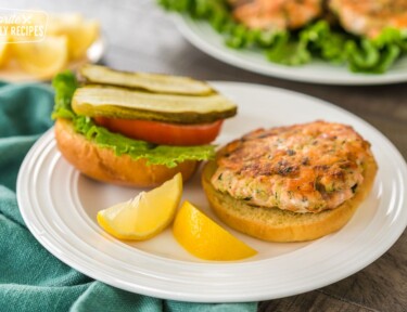 A salmon patty on a burger with salmon patties in the background