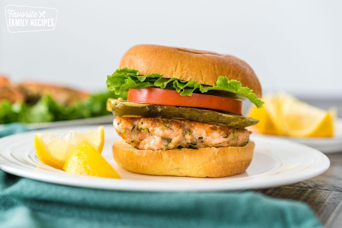 A salmon patty served on a burger with lettuce, tomato, and pickle