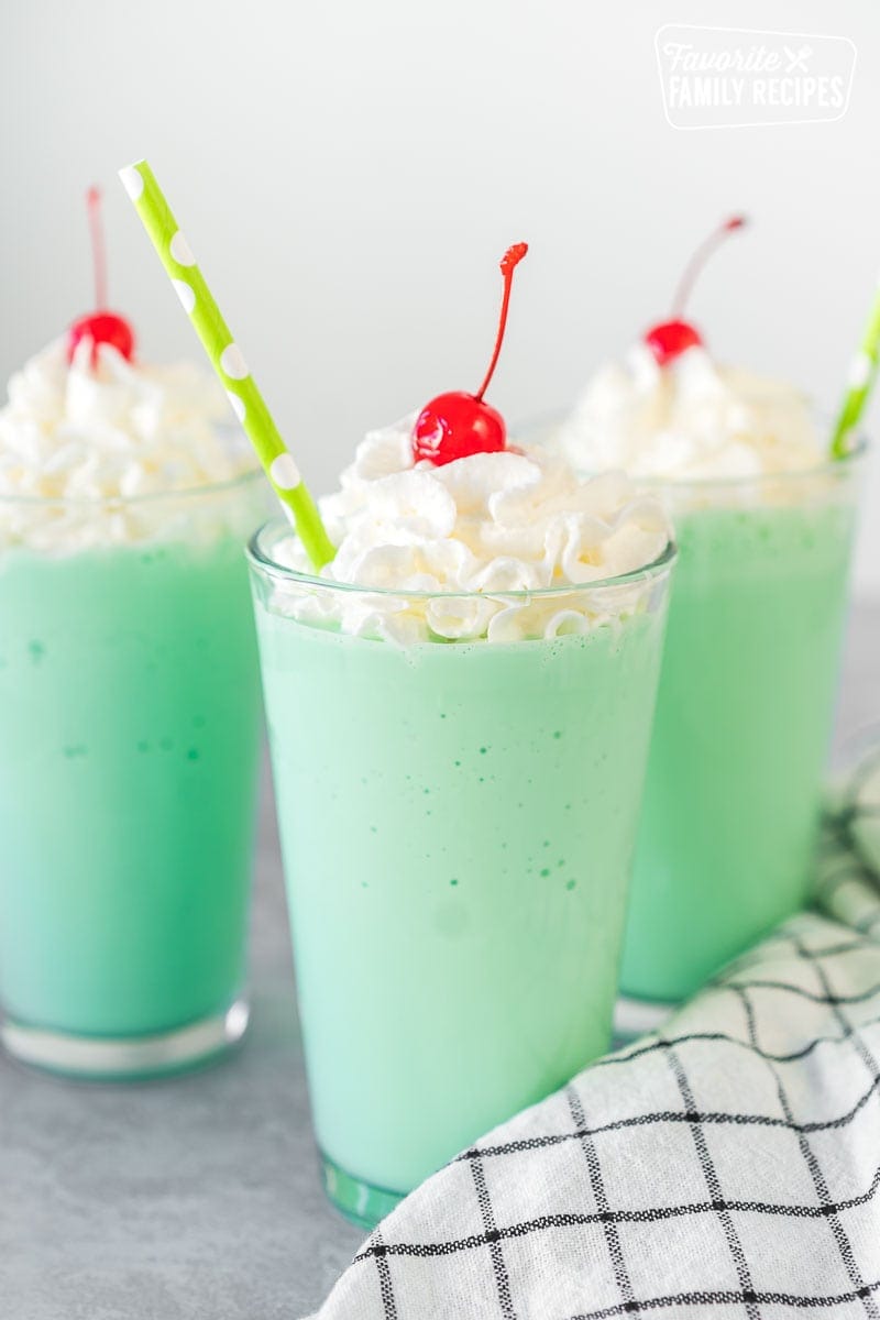 A mint green Shamrock shake in a clear glass topped with whipped cream, a maraschino cherry, and a straw.