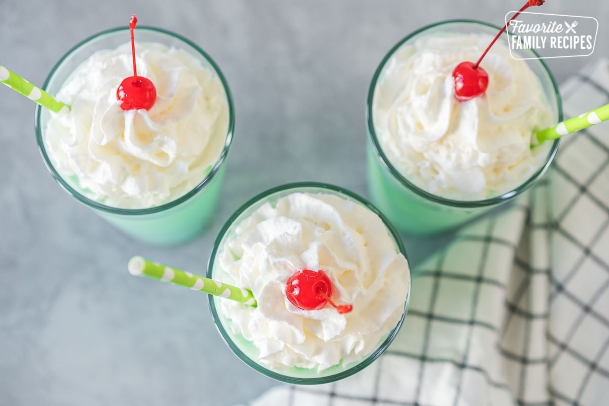 A mint green Shamrock shake in a clear glass topped with whipped cream, a maraschino cherry, and a straw.