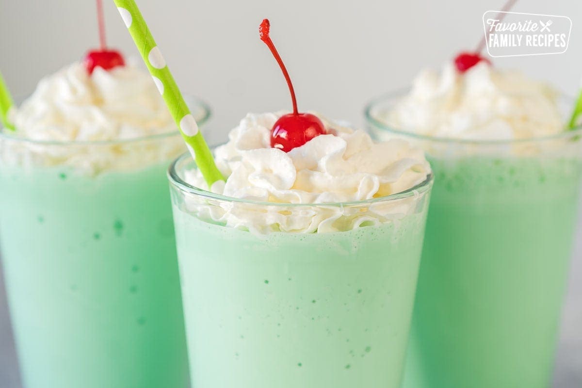 A mint green Shamrock shake in a clear glass topped with whipped cream, a maraschino cherry, and a straw.