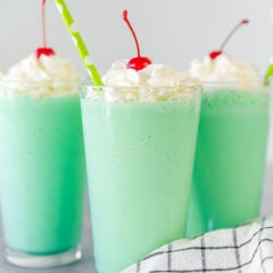 A mint green Shamrock shake in a clear glass topped with whipped cream, a maraschino cherry, and a straw.