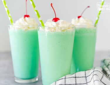 A mint green Shamrock shake in a clear glass topped with whipped cream, a maraschino cherry, and a straw.