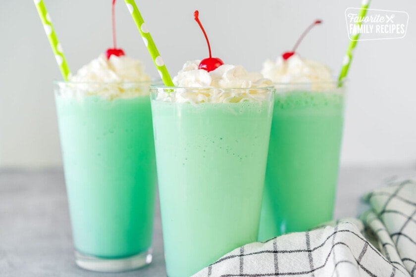 A mint green Shamrock shake in a clear glass topped with whipped cream, a maraschino cherry, and a straw.