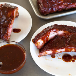 smoked ribs on two plates with a side of bbq sauce