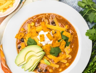 Cafe Zupas Chicken Enchilada Chili in bowl with lime, cheese, avocado, cilantro and sour cream on side.