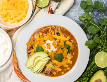 Cafe Zupas Chicken Enchilada Chili in bowl with lime, cheese, avocado, cilantro and sour cream on side.