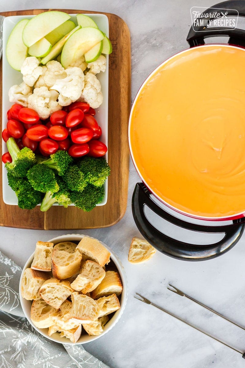 Top view of cheddar fondue with sliced apples, cauliflower, tomatoes and broccoli on the side for dipping.