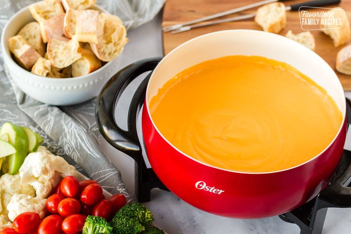 Side view of warmed cheddar fondue with bread and vegetables for dipping.