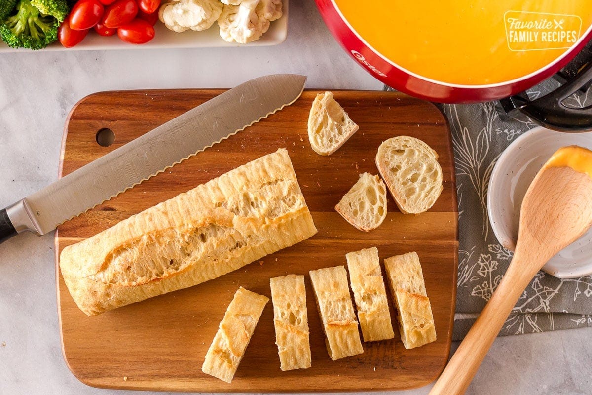 Sliced bread on a cutting board with cheddar fondue and vegetables on a platter.