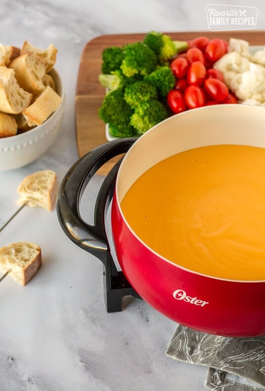 Fondue pot with Cheddar cheese fondue, bowl of sliced French bread and tray of vegetables.