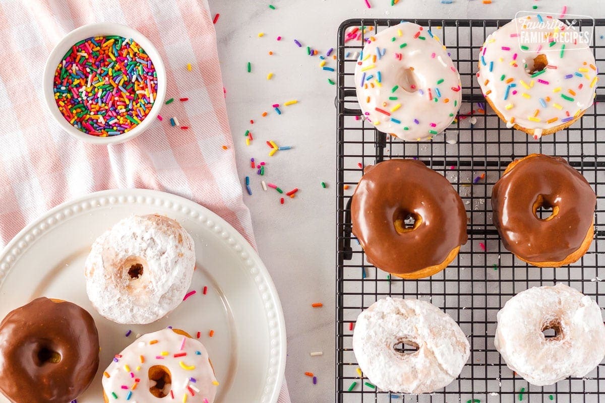 Cronuts decorated on a cooling rack and a plate with sprinkles, chocolate and powdered sugar.