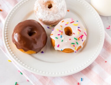 Three cronuts on a serving plate with a cup of milk.