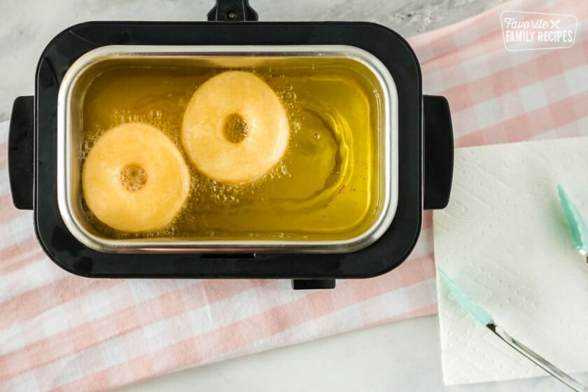 Two cronuts frying in oil in a deep fryer