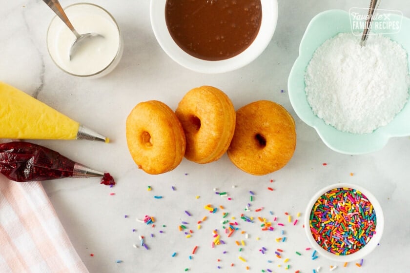 Cronuts surrounded by toppings including raspberry filling, chocolate, and sprinkles