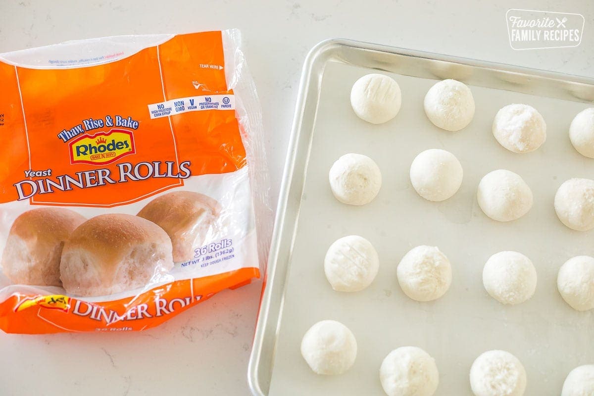 Frozen dinner rolls on a parchment lined baking sheet next to a bag of frozen rolls